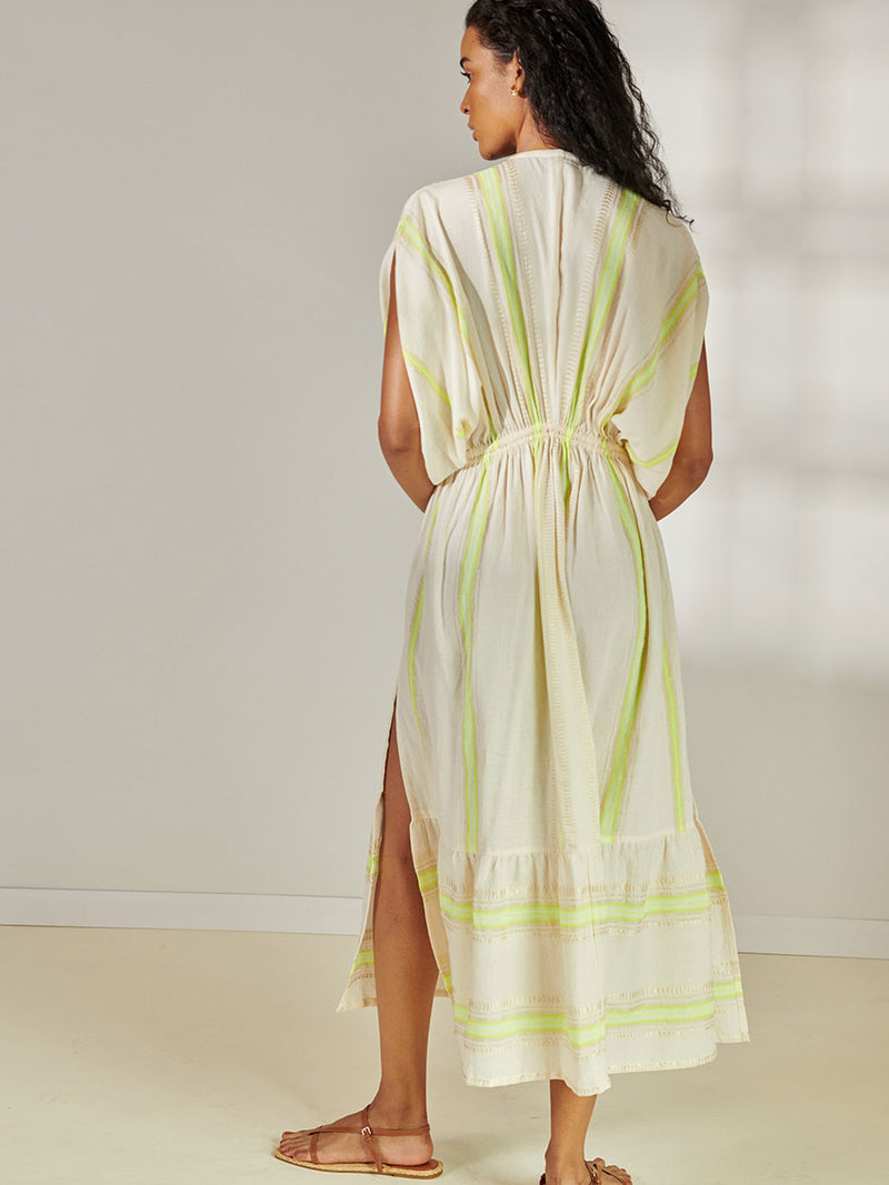 Back view of a Woman Standing Wearing lemlem Leila Plunge Neck Dress featuring combination of matte and shine natural tibebs and stripes in Vanilla Cream and Lime sorbet colors.