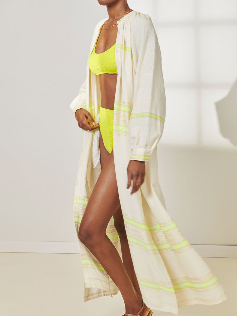 Close Up View of a Woman Standing Wearing lemlem Makeda Button Up Dress featuring combination of matte and shine natural tibebs and stripes in Vanilla Cream and Lime sorbet colors.