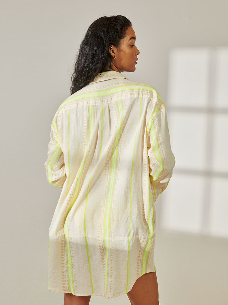 Back View of a Woman Standing Wearing lemlem Mariam Shirt featuring combination of matte and shine natural tibebs and stripes in Vanilla Cream and Lime sorbet colors