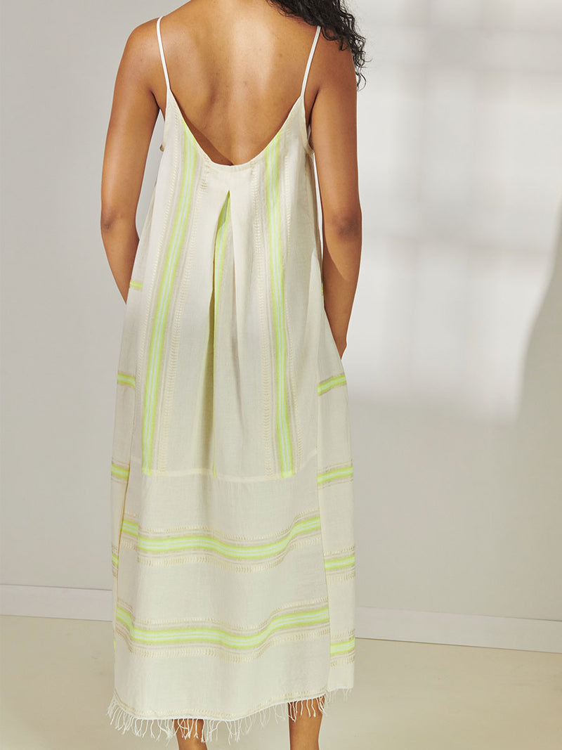 Back View of a Woman Standing Wearing lemlem Nia Slip Dress featuring combination of matte and shine natural tibebs and stripes in Vanilla Cream and Lime sorbet colors.