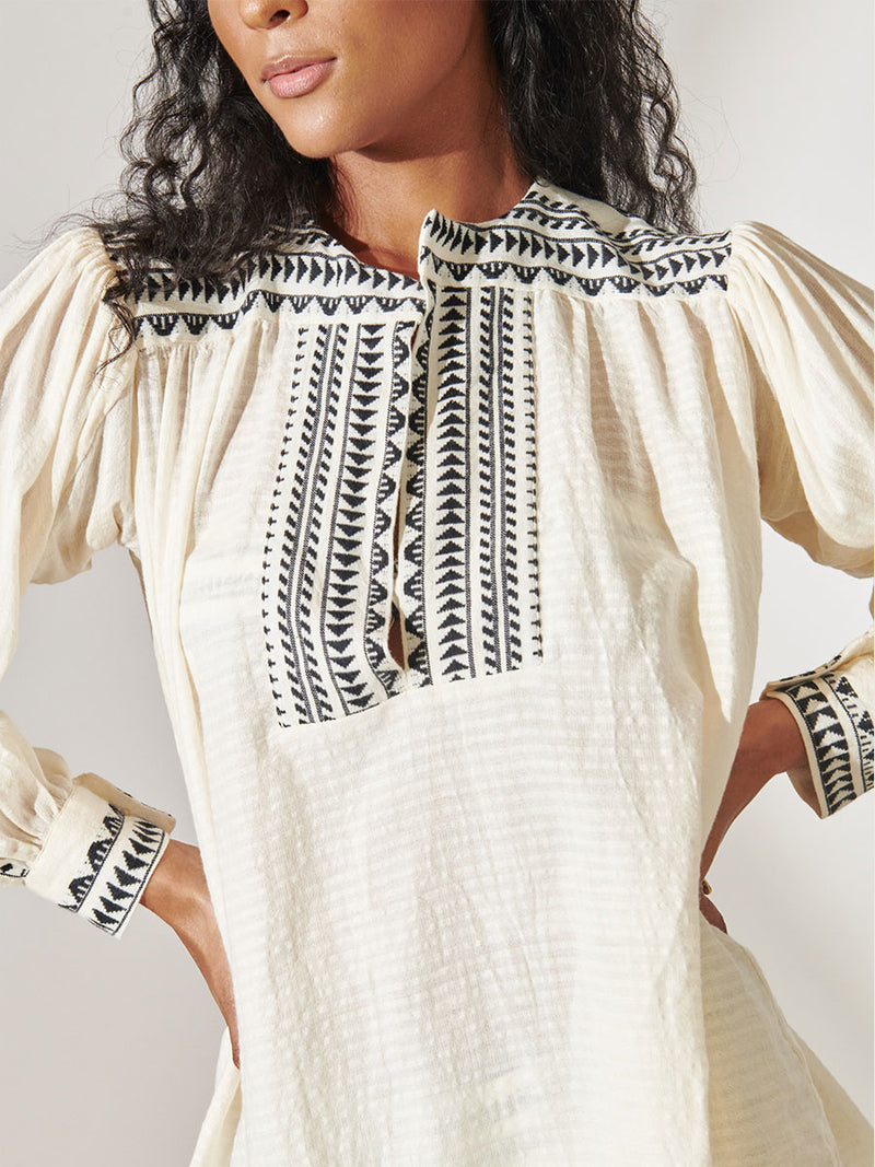Close up on a Woman Standing Wearing Dera Blouse featuring intricate black Tibeb bands on a textured vanilla background 