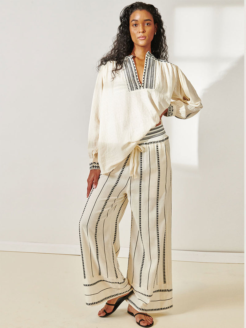 Woman Standing Wearing Dera Blouse featuring intricate black Tibeb bands on a textured vanilla background and matching Desta Pants