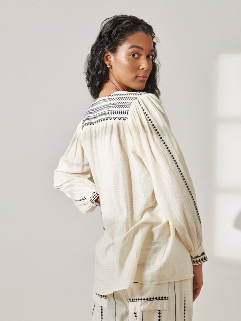 Back View of a Woman Standing Wearing Dera Blouse featuring intricate black Tibeb bands on a textured vanilla background and matching Desta Pants