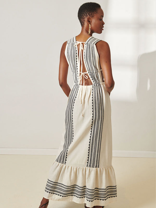 Back View of a Woman Standing Wearing lemlem Lelisa V Neck Dress featuring intricate black Tibeb bands on a textured vanilla background.