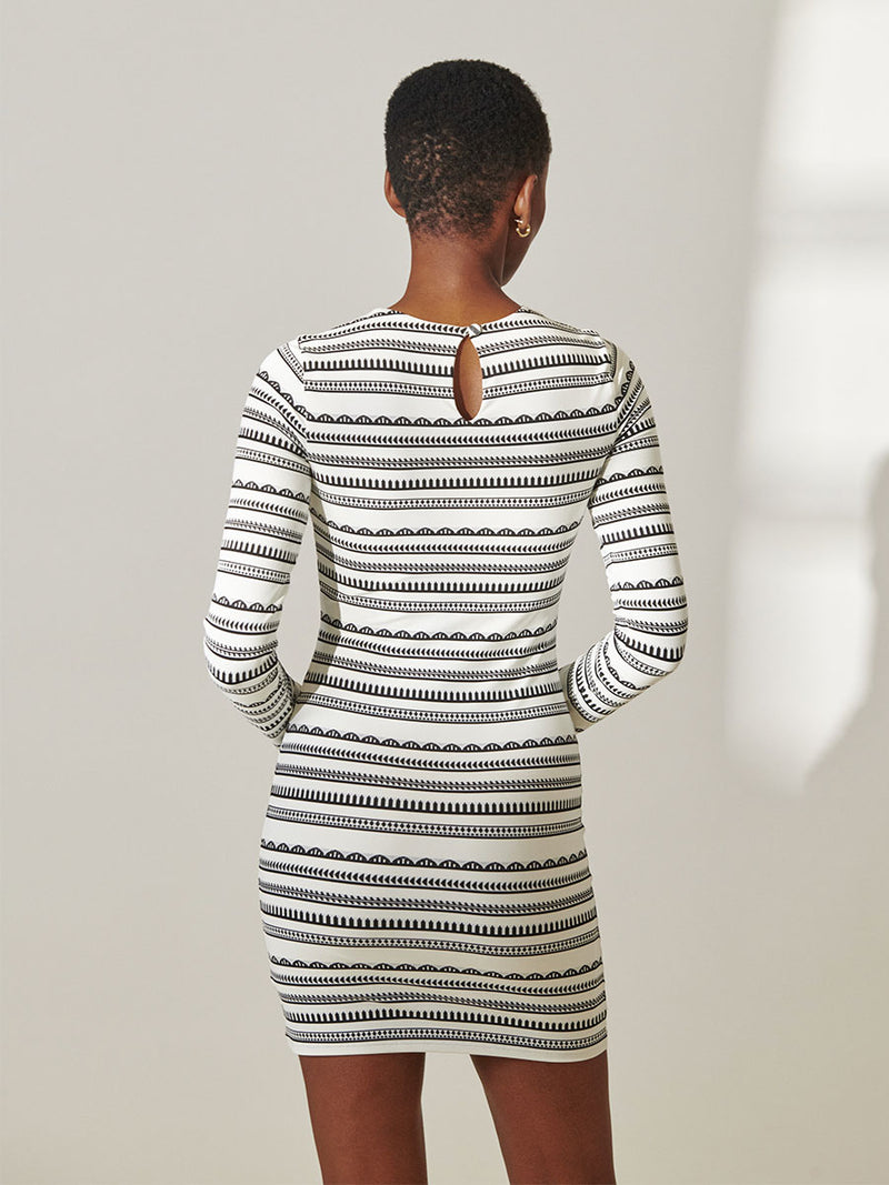 Back View of a woman standing wearing lemlem Nyala Swim Dress featuring intricate black Tibeb bands on a textured white background.