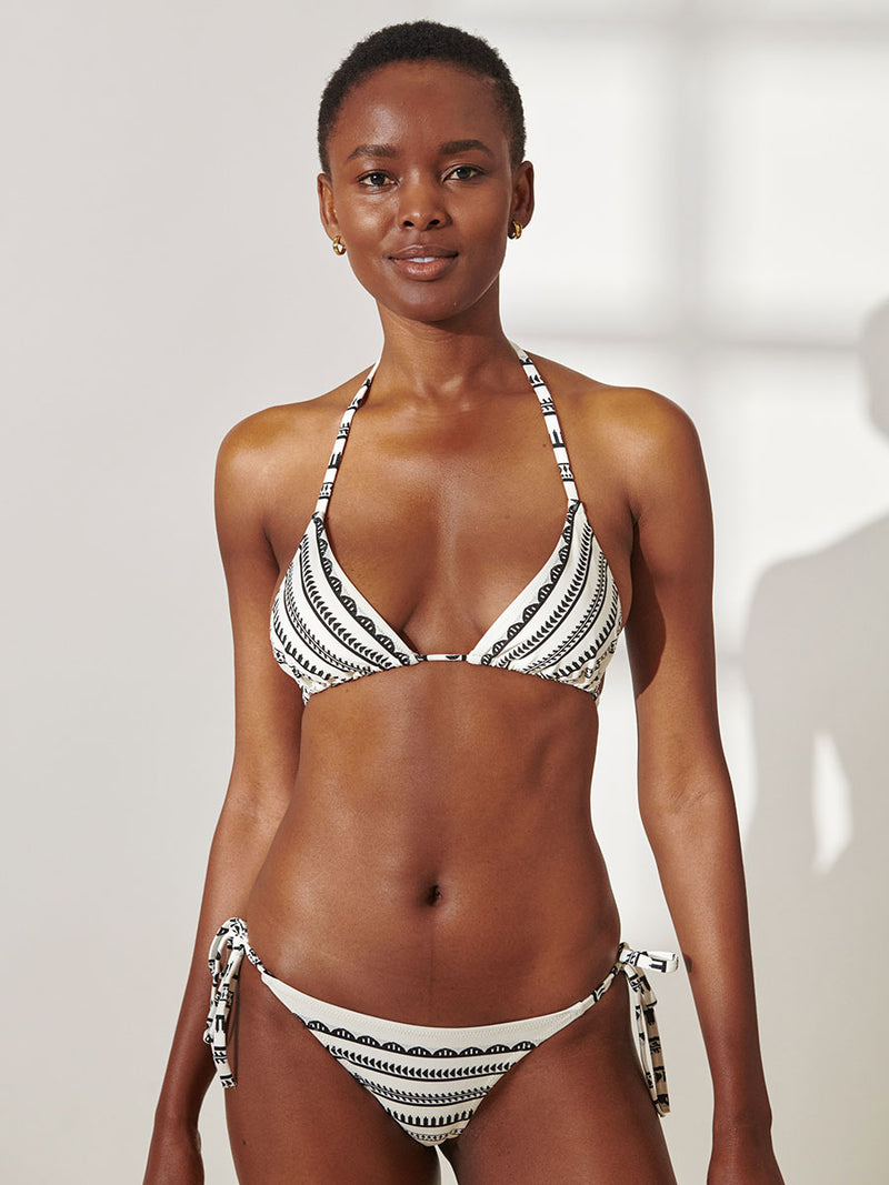 Woman Standing Wearing lemlem Rekka String Bikini Bottom featuring intricate black Tibeb bands on a textured white background and matching Triangle Top