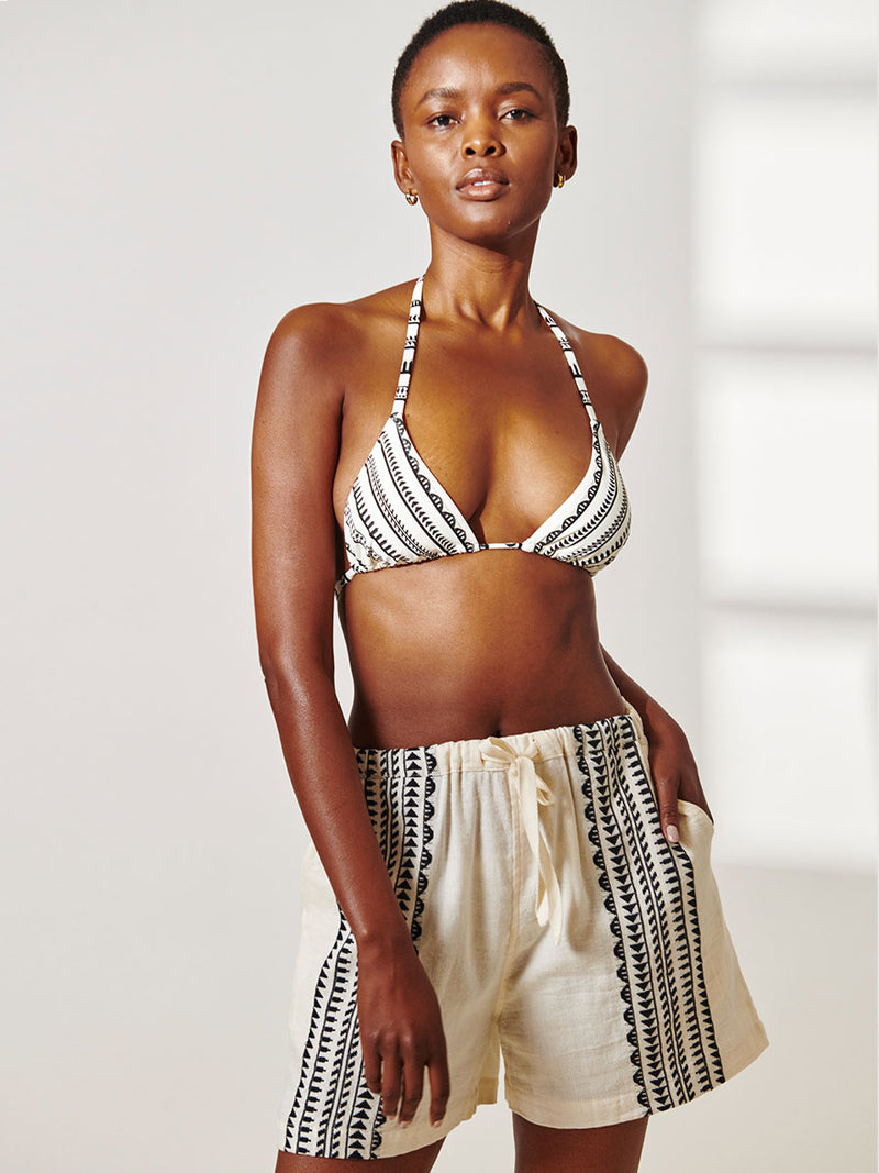 Woman Standing Wearing lemlem Safia Shorts featuring intricate black Tibeb bands on a textured vanilla background and Matching Triangle Top