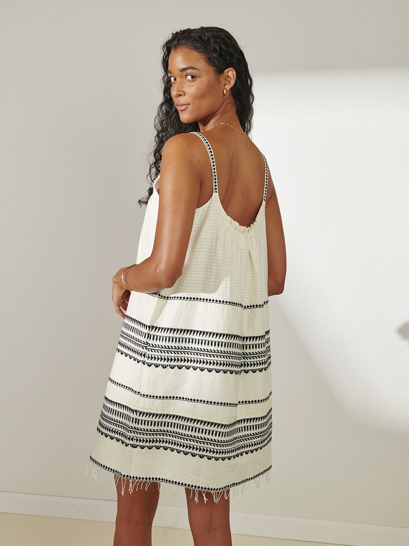 Back View of a Woman Standing Wearing lemlem Zina Swing Dress featuring intricate black Tibeb bands on a textured vanilla background.