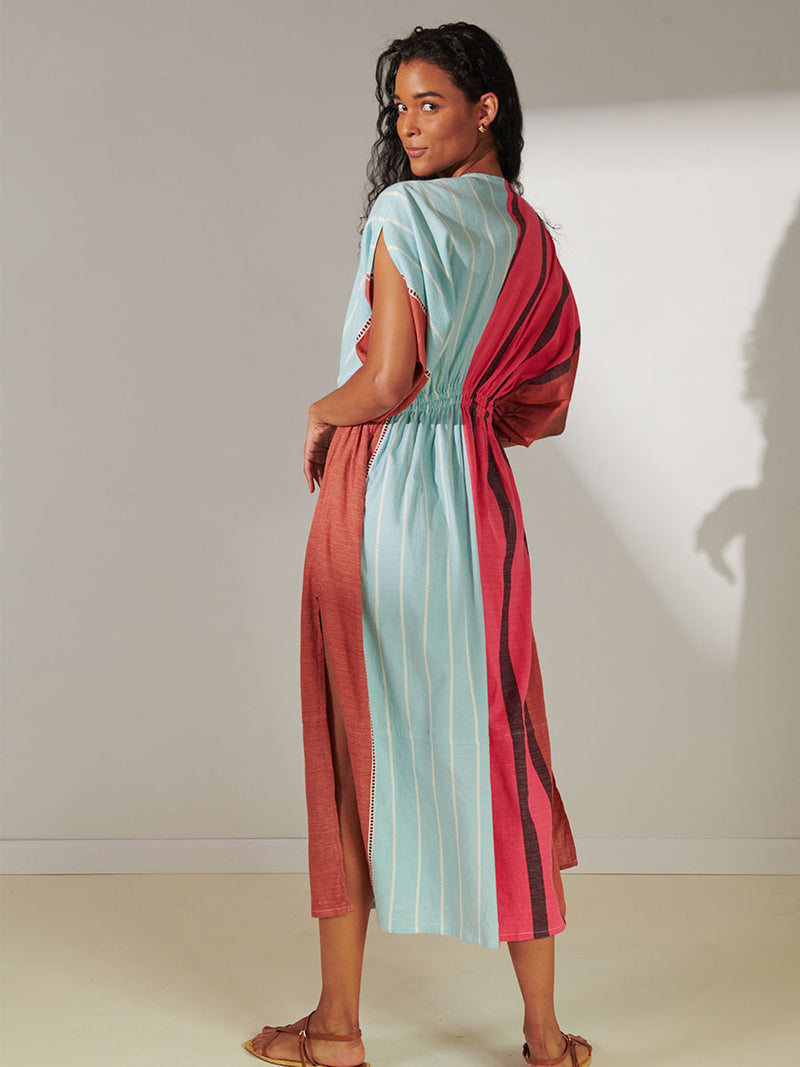 Back View of a Woman Standing Wearing Lelia Plunge Neck Dress Featuring all over stripe color block pattern in sky, terracotta, brick and burgundy colors.