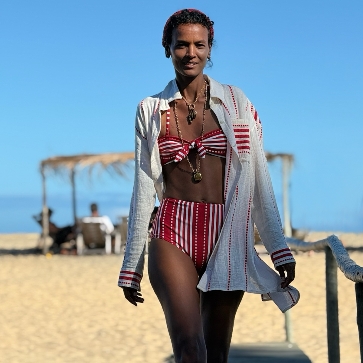 Liya Kebede in a red and white striped lemlem swimsuit with a matching handwoven lemlem shirt on a beach