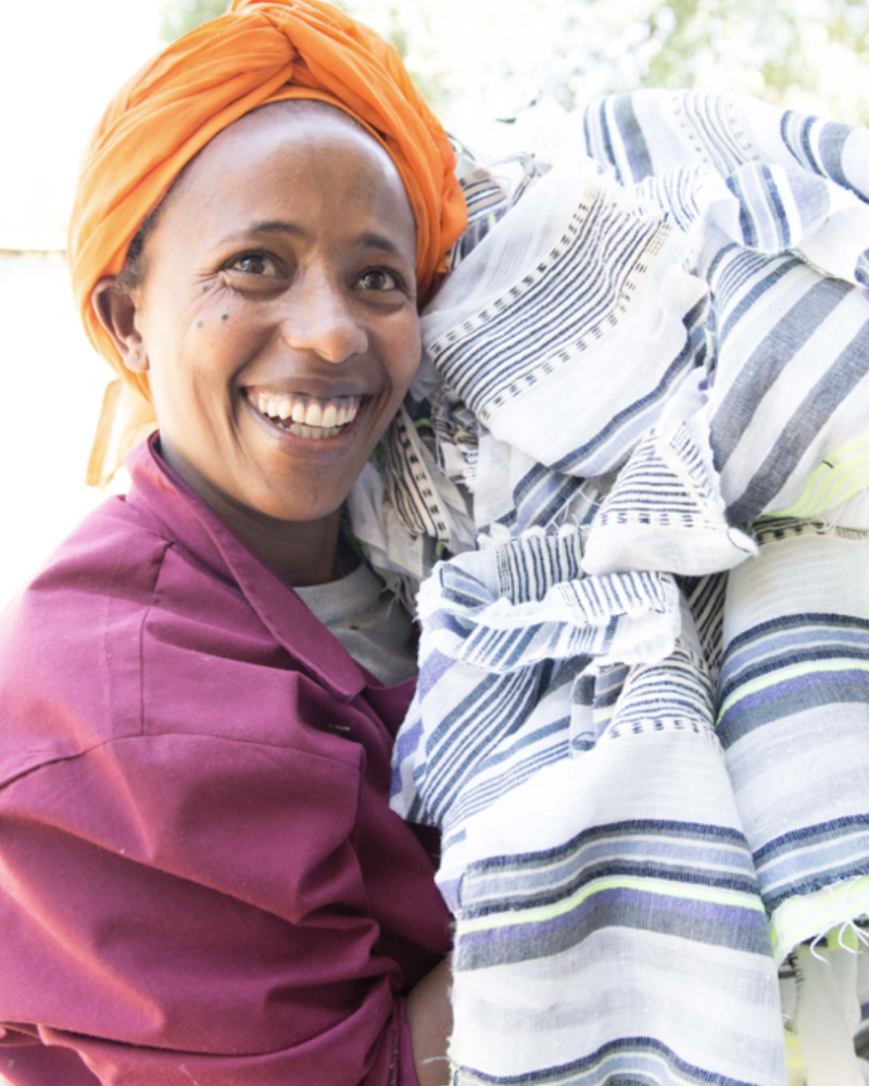 Smiling woman artisan carrying a pile of hand-woven colorful fabric