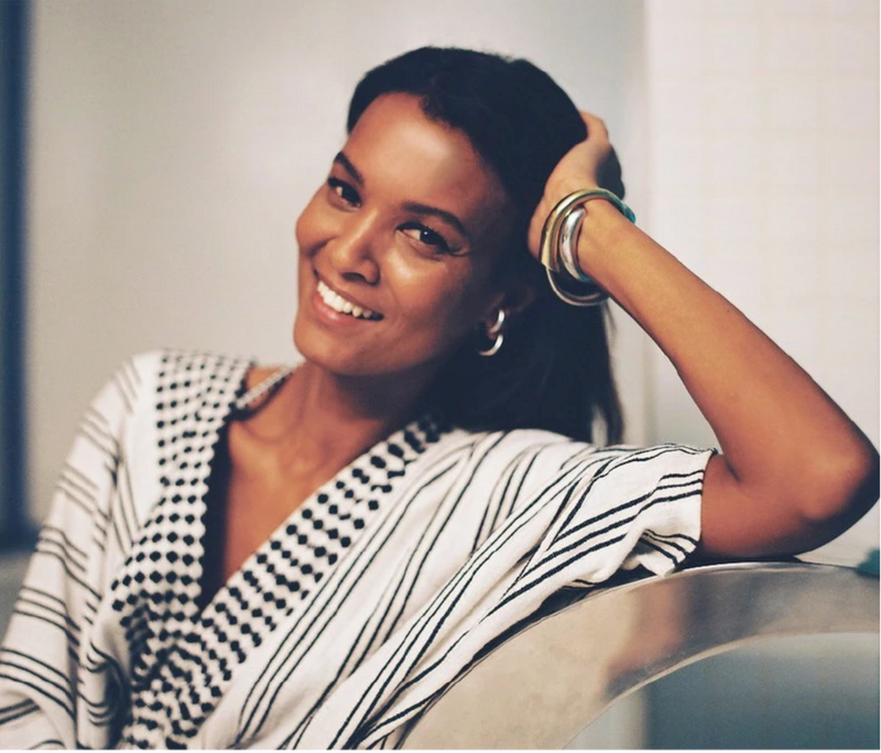 Portrait of lemlem's founder Liya Kebede sitting on a chair and wearing a black and white maxi dress