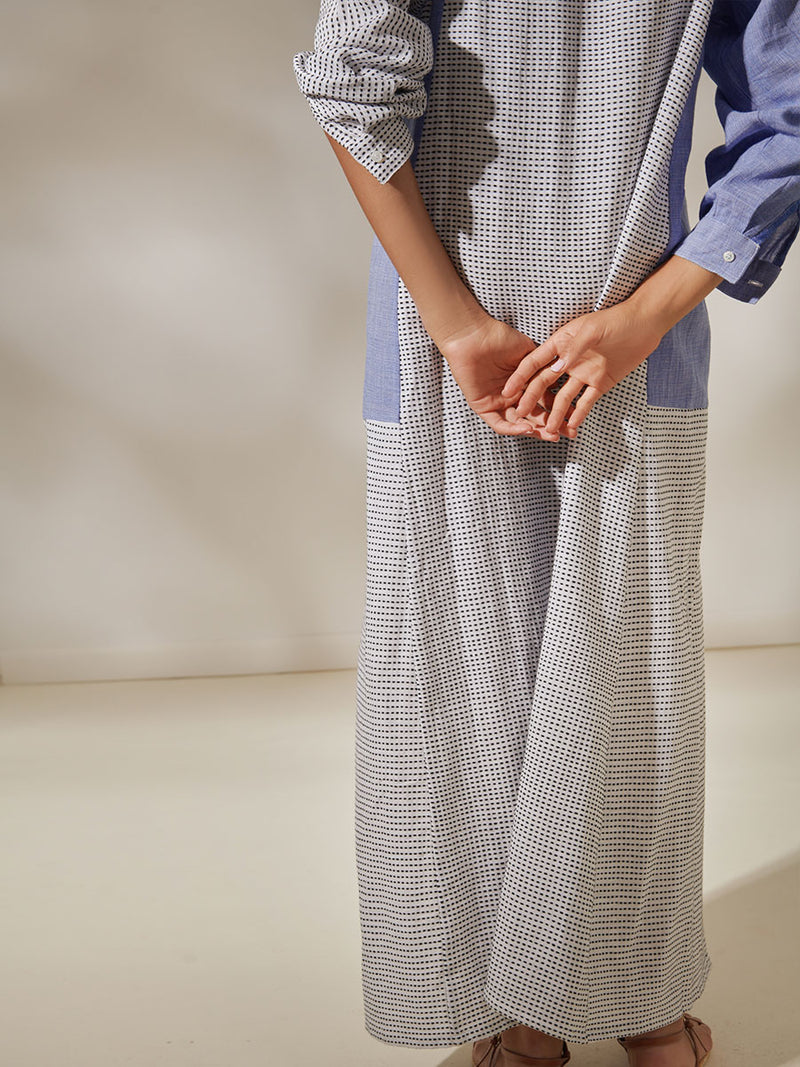 Back View of a Woman Standing Wearing Makeda Button Up Dress Featuring textural dot pattern that contrasts the asymmetrical color-blocking of denim blues.