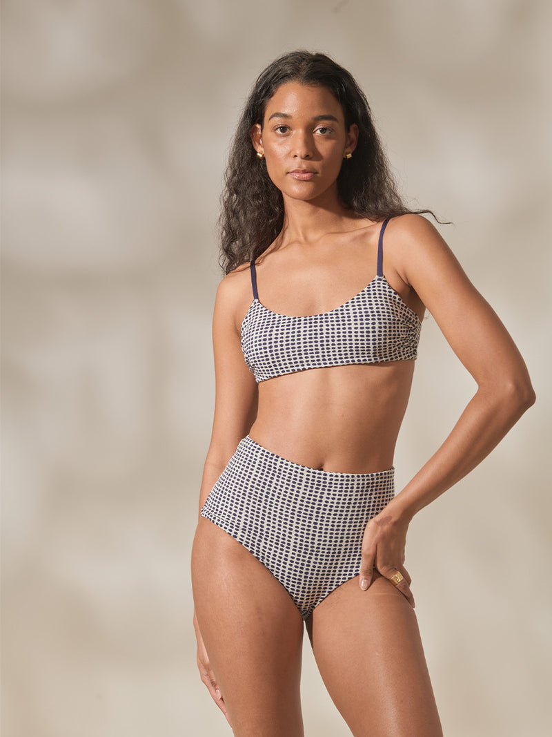 Woman Standing Wearing Sisay Blue Asha Scoop Top and High Waist Bikini Bottom Featuring Blue Dotted Pattern