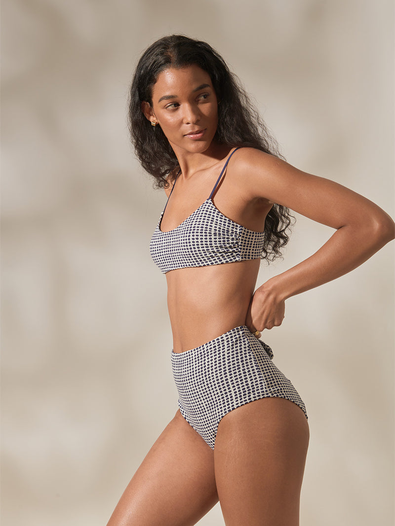 Woman Standing Wearing Sisay Blue Asha Scoop Top and High Waist Bikini Bottom Featuring Blue Dotted Pattern
