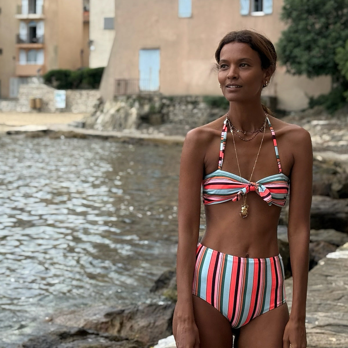 Liya Kebede standing wearing lemlem bikini swimsuit featuring striped pattern in multiple colors