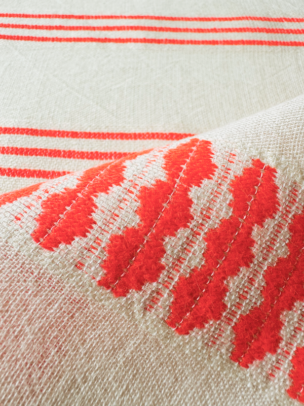 close up om lemlem tigist flame fabric featuring intricate electric orange toned Tibeb pattern on a cream biscuit background.