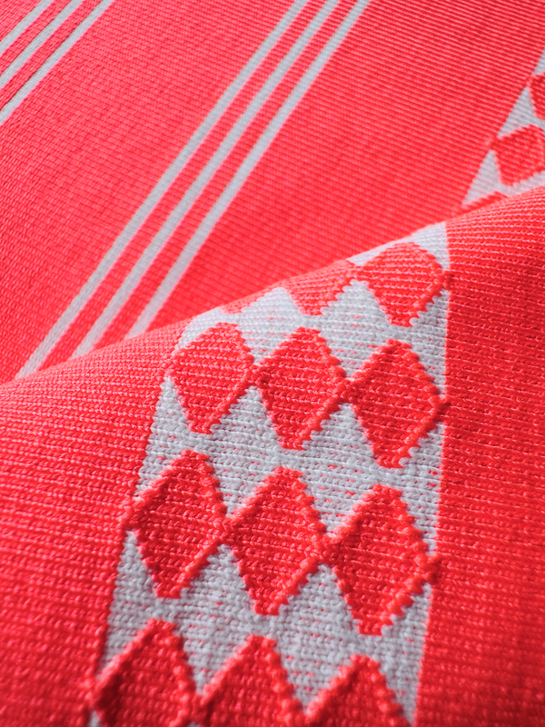 close up on lemlem tigist flame swim fabric featuring intricate ivory Tibeb pattern on a bright coral pink background 