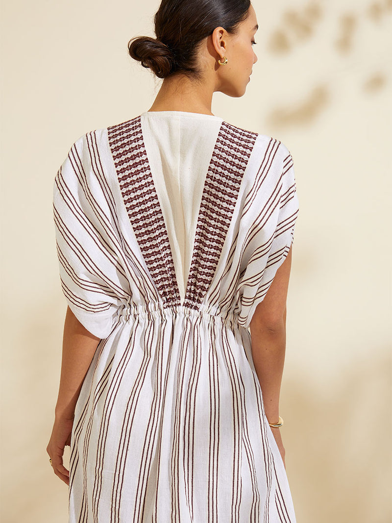 Back view of a woman standing wearing the Tigist Plunge Neck Dress featuring earthy brown tibeb diamond design bands on a white background.  