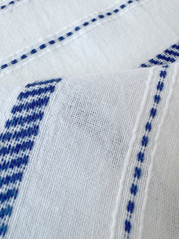 close up on lemlem fabric  featuring crisp white woven with diagonal dotted stripes in bright blue and a subtle textured weave
