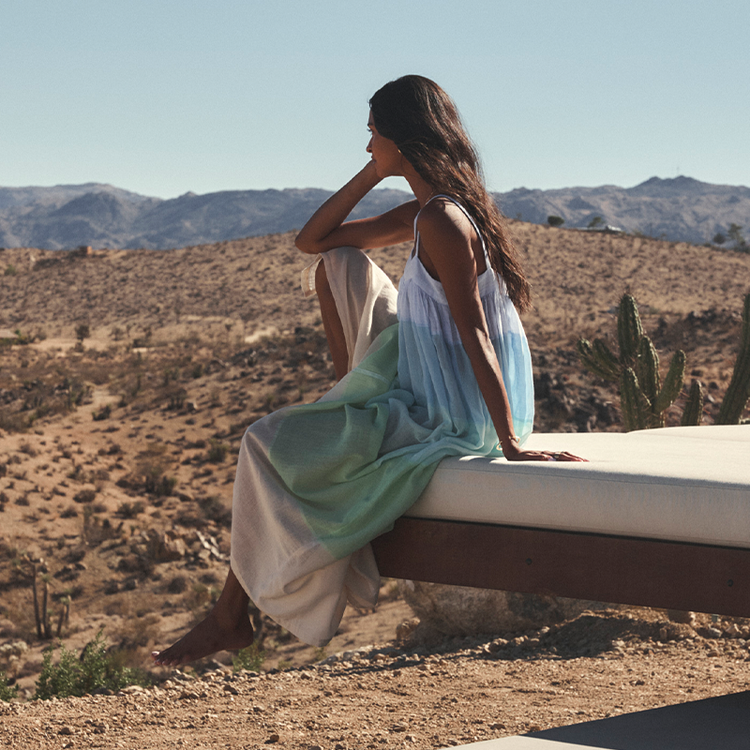 Woman sitting on sunbathing bed in a desert landscape with mountains in the background