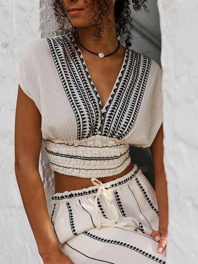 Close up on a Woman Sitting Wearing Alia Plunge Top featuring intricate black Tibeb bands on a textured vanilla background and matching Desta Pants