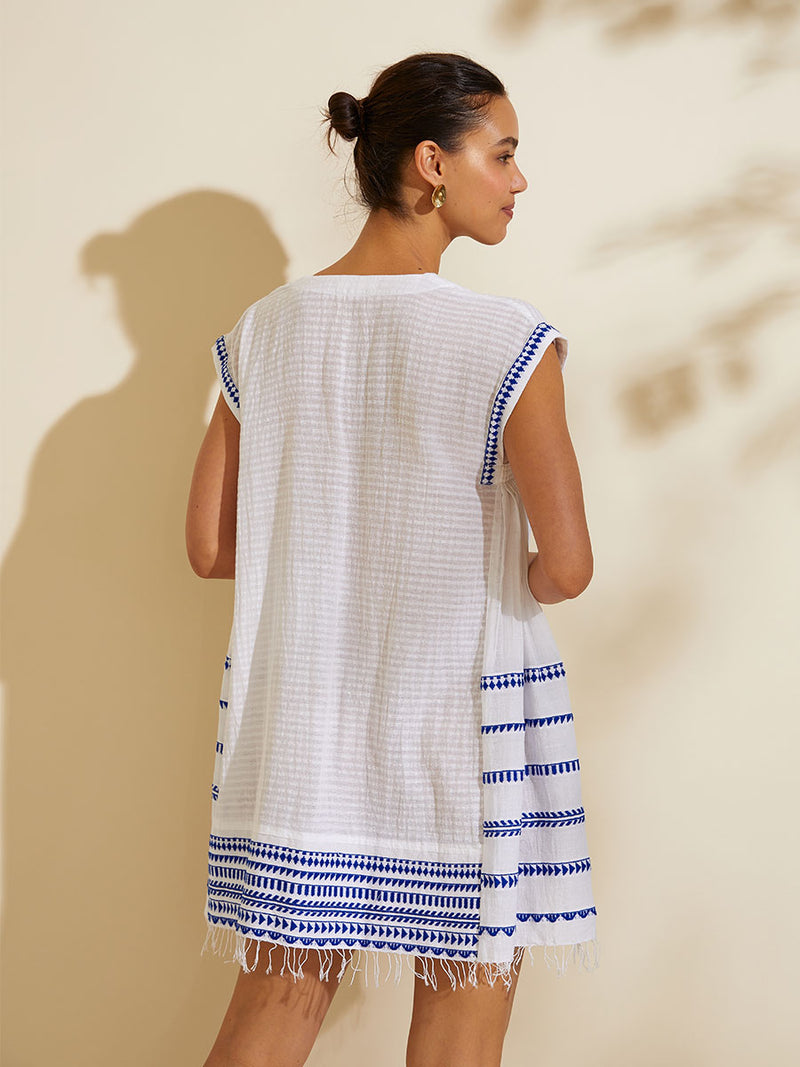 Back view of a woman standing wearing the Yani Caftan Dress featuring blue tibeb diamond design bands on a textured seersucker white background.  