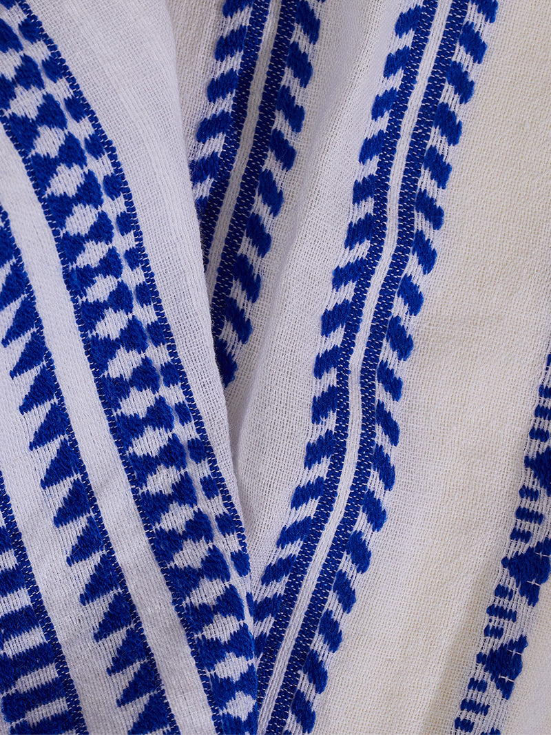 Close up on the fabric of the Yani Plunge Neck Dress featuring blue tibeb diamond design bands on a textured seersucker white background.  