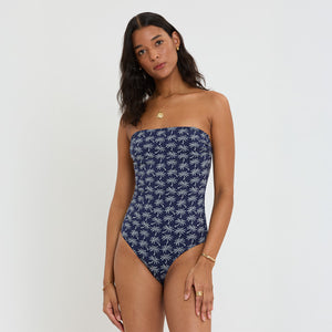 Woman wearing a strapless navy blue lemlem swimsuit with white palm tree pattern on a white background