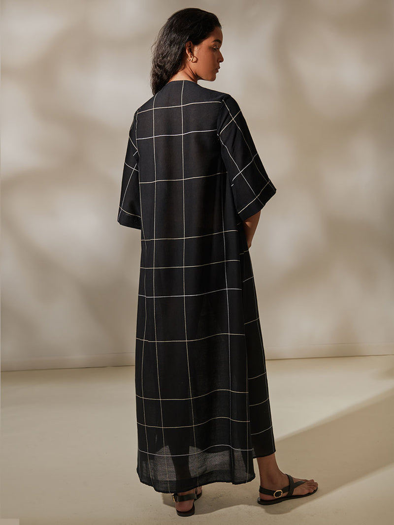 Back View of a Woman Standing Wearing Edna V Neck Maxi Dress featuring Big White Plaid Patten on Black Cotton Background