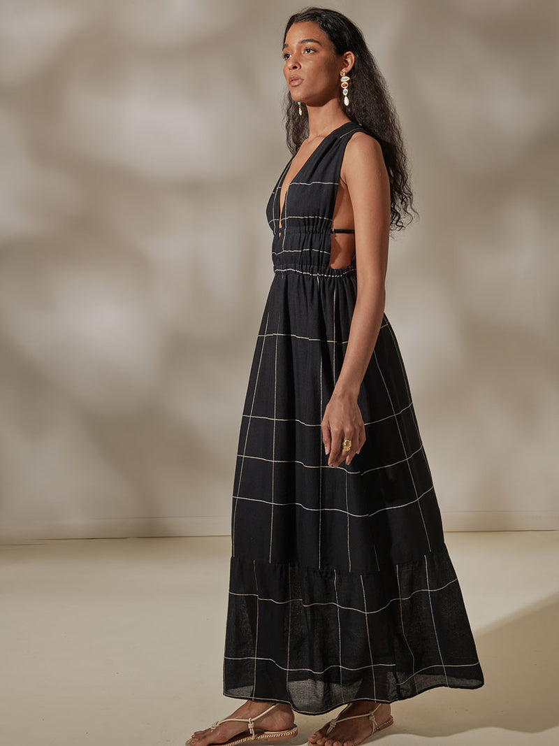 Side View of a Woman Standing Wearing Lelisa V Neck Maxi Dress featuring Big White Plaid Patten on Black Cotton Background