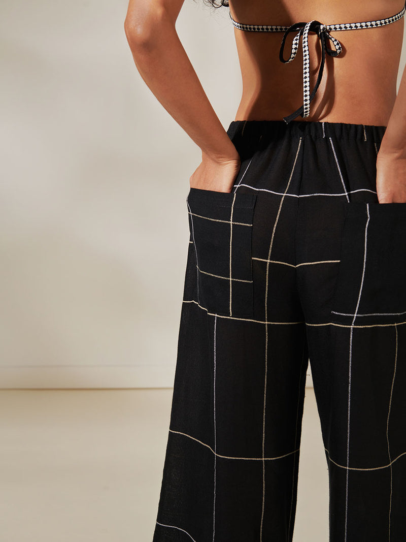 Back View of a Woman Standing Wearing Desta Wide Leg Pants featuring big white plaid pattern on black cotton background