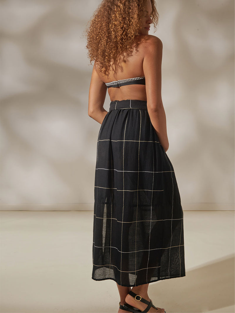 Back View of a Woman Standing Wearing Lena Black Bandeau Top and Tola Maxi Skirt featuring Big White Plaid Patten on Black Cotton Background