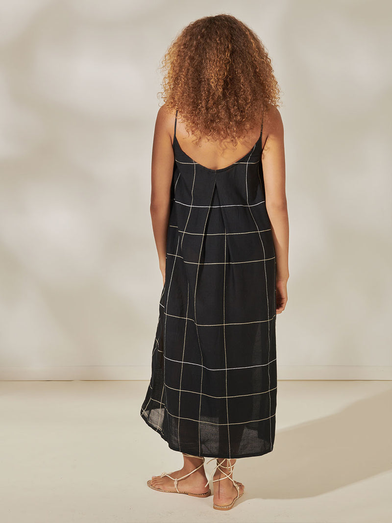 Back View of a Woman standing wearing Nia Maxi Slip Dress featuring Big White Plaid Pattern on Black Cotton Background