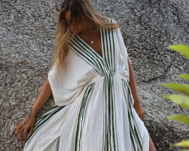 Woman standing in front of a rock wearing a white Eshe Plunge Neck maxi plunge neck dress with dark green olive stripes