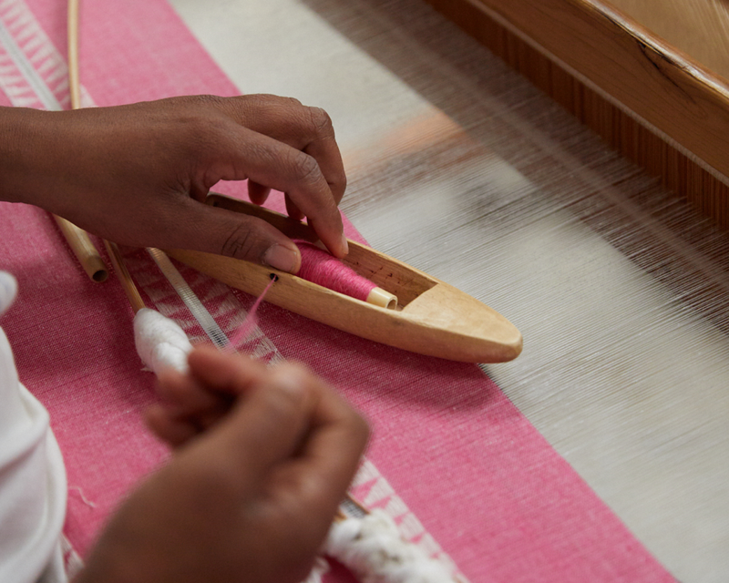 Close up of the hands of an artisan in Ethiopia weaving by hand on a loom a pink fabric