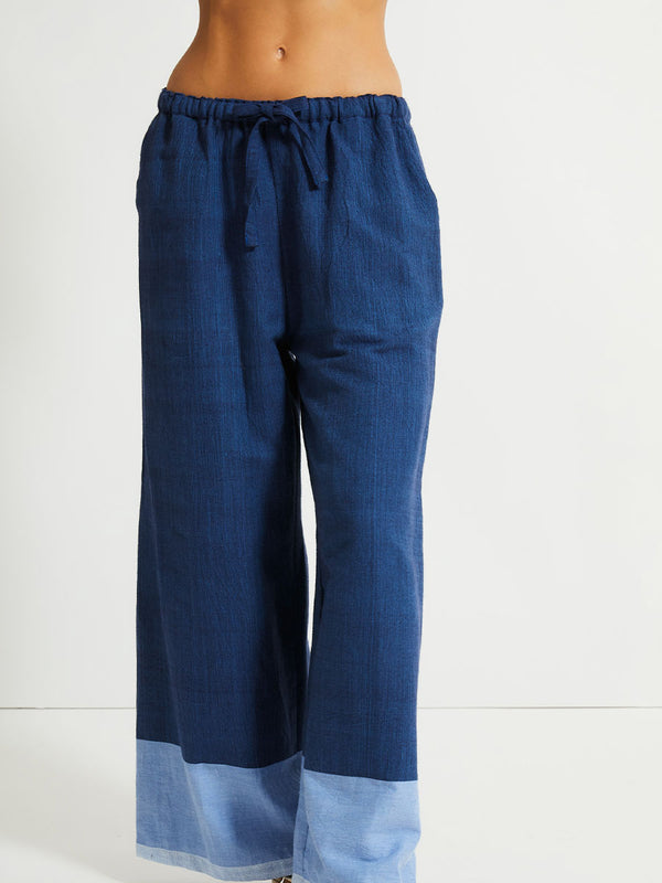 Close up on a Woman Standing Wearing lemlem Desta Pants featuring a striking color-block combination of three shades of blue, paired with bands of neutral cream and white, inspired by handmade indigo quilting and African textil.
