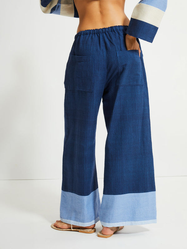 Close up on a back of a  Woman Standing Wearing lemlem Desta Pants, Terrara Jacket and blouse featuring a striking color-block combination of three shades of blue, paired with bands of neutral cream and white, inspired by handmade indigo quilting and African textil.