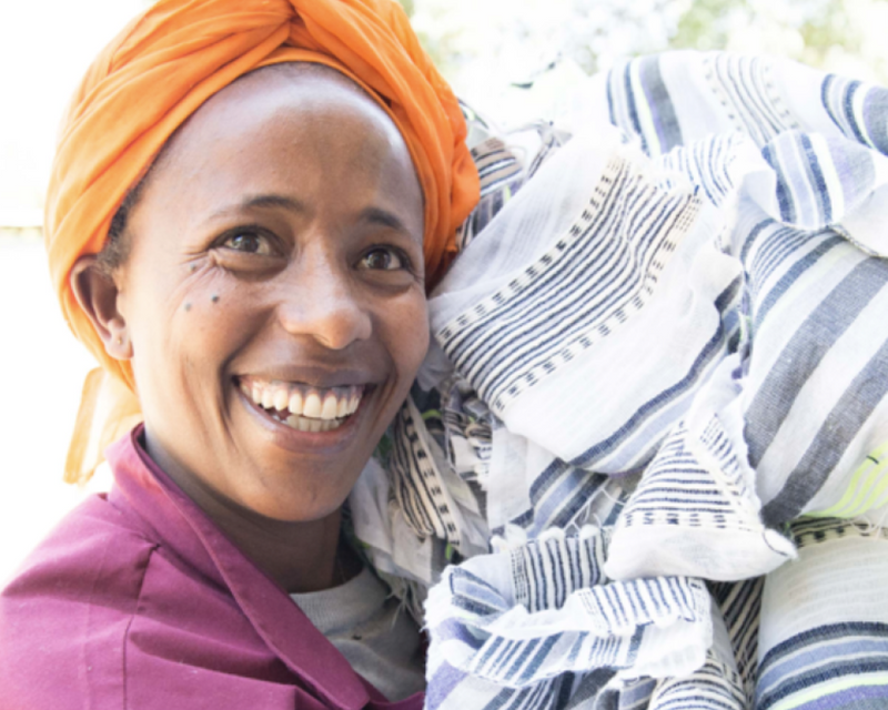 Close up of a smiling woman artisan carrying a pile of hand-woven fabrics