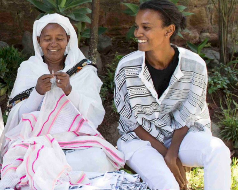 Our founder Liya Kebede and a woman artisan sitting on a bench outside in Ethiopia