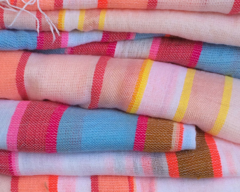 A pile of folded stripy and colorful hand-woven fabrics