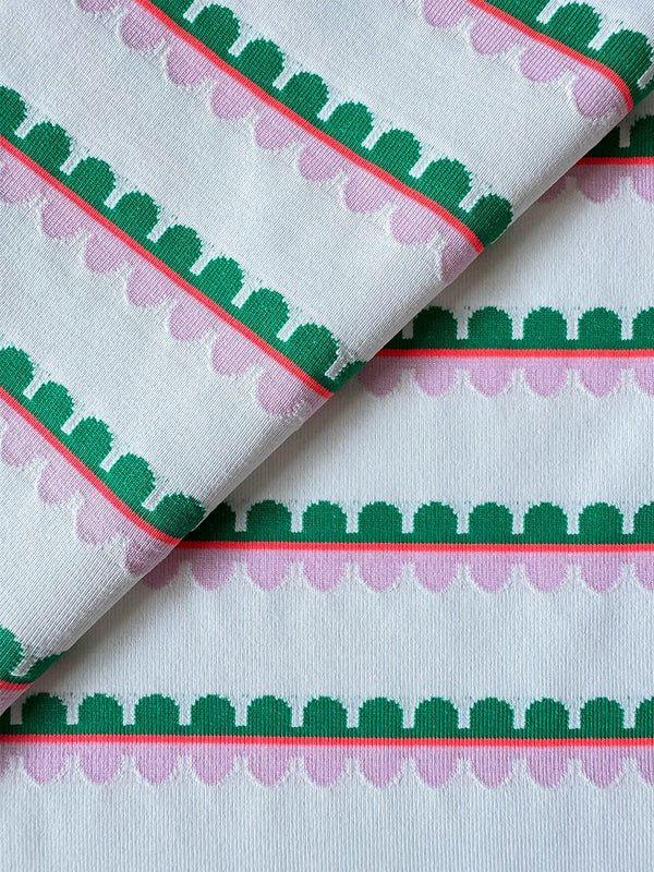 Close up on lemlem Kibebi Fragaria Fabric featuring a playful, preppy scalloped Tibeb weave with vibrant green, soft pink, and fiery red accents.

