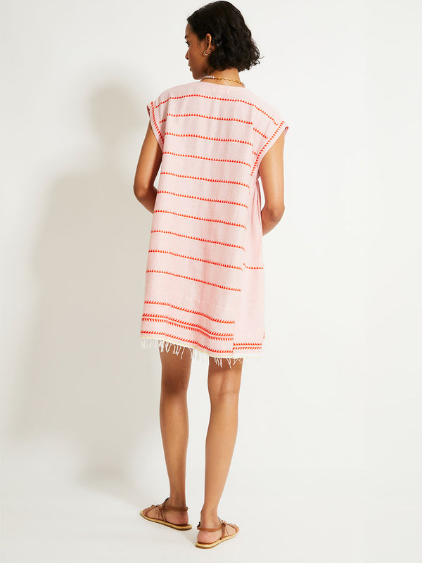 Back of a Woman Standing Wearing lemlem ELINA Caftan featuring vibrant orange red Tibeb pattern on a soft antique rose pink background, with a hint of citron tipping.