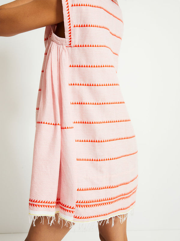 Side View of a Woman Standing Wearing lemlem ELINA Caftan featuring vibrant orange red Tibeb pattern on a soft antique rose pink background, with a hint of citron tipping.