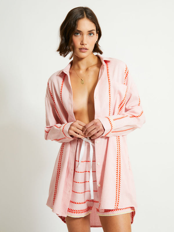 Woman Standing Wearing lemlem SAFIA Shorts  featuring vibrant orange red Tibeb pattern on a soft antique rose pink background, with a hint of citron tipping and a matching shirt