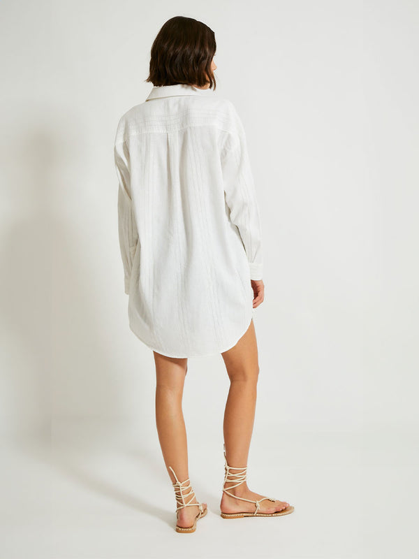 Back Shot of a Woman Standing Wearing lemlem MARIAM Shirt featuring white color and shorts featuring striped and dotted pattern on silky navy background