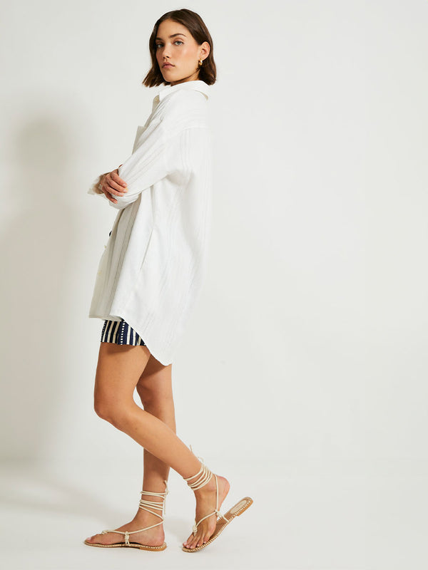 Side Shot of a Woman Standing Wearing lemlem MARIAM Shirt featuring white color and shorts featuring striped and dotted pattern on silky navy background