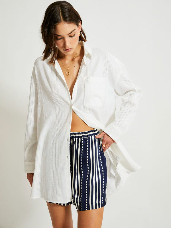 Woman Standing Wearing lemlem MARIAM Shirt featuring white color and shorts featuring striped and dotted pattern on silky navy background