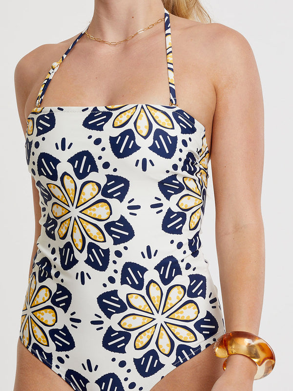 Woman Standing wearing lemlem DINHA One Piece featuring exclusive in-house–designed floral prints accented by ancient motifs, rendered in bright yellow and navy on an ivory background.