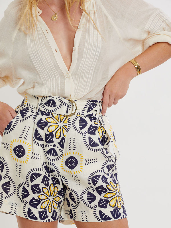 Woman standing wearing lemlem linen FAIZAH Shorts featuring floral inspired pattern and handwoven MITA Blouse in sheer fabric in cream color